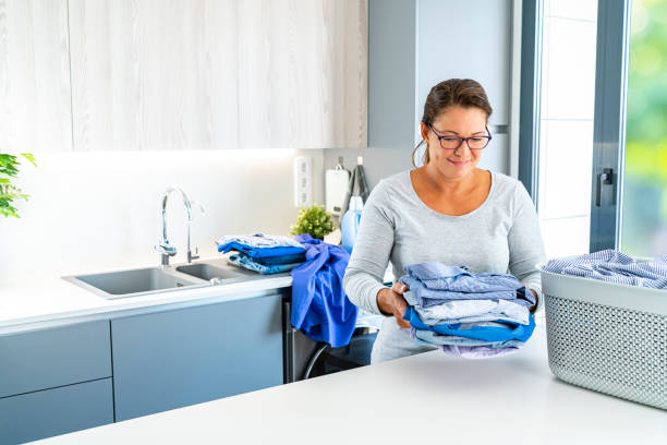 Une auxiliaire de vie tenant des vêtements propres pliés après la machine à laver.