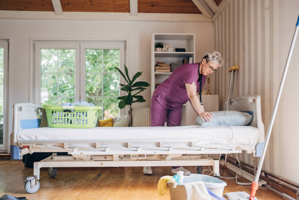 Entretien du domicile : Une aide à domicile en blouse violette est vue en train de faire un lit et un panier de linge propre est posé sur le lit